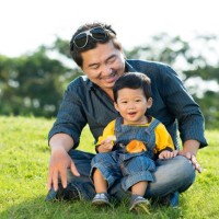 Asian man and his little son sitting on the grass