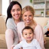 Female couple sit together with their son in their home and all smile for the camera