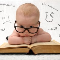 funny portrait of cute baby in glasses lieing on old book and thinking of all the knowledge in the world