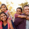 Mixed race parents carry their kids piggyback in a park