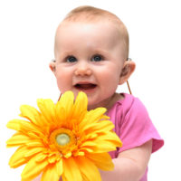 Cute baby girl sits against white background holding large yellow flower